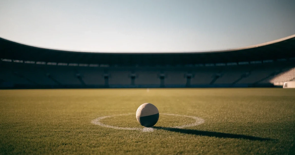Uma bola de futebol no ponto central de um relvado, à luz da manhã
